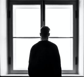 solitude, lonely man staring through a window from a bleak and dark inside
